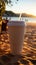 Close up plastic white coffee cup with black straw on sand of beach at sunset or sunrise sunlight