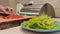 A close-up of a plate of finely chopped green paprika. against the background of female hands slicing tomatoes