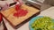 A close-up of a plate of finely chopped green paprika. against the background of female hands slicing tomatoes