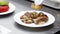 Close-up of a plate with fried mushrooms on the kitchen table. The cook lays out the food with the chef`s tongs
