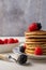 Close-up of plate with pancakes with blackberries and raspberries, fork with blackberries, on white wooden table and bowl with ras