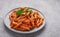 Close-up of a plate with Penne All`arrabbiata pasta on a grey background
