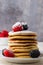 Close-up of plate with stacked pancakes, with blackberries, raspberries and sugar, on white wooden table, bowl with out-of-focus r