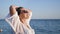 Close-up pleasant tanned relaxed girl in white shirt raising hand enjoying freedom at sea background