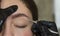 Close-up plucking young woman face eyebrows with tweezers during eyebrow correction in beauty salon