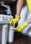 Close up Plumber in yellow household gloves changes water filters. Repairman changing water filter cartridges in kitchen