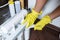 Close up Plumber in yellow household gloves changes water filters. Repairman changing water filter cartridges in kitchen