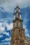 Close-up of pointed bell tower church made of bricks and golden clock under blue sky in Amsterdam.