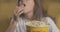 Close-up of popcorn box with blurred young Caucasian woman eating snack at the background. Positive cinema visitor