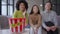 Close-up of popcorn bucket with three blurred young multinational women watching TV at background talking and laughing