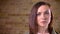 Close-up portait of young beautiful brown-headed woman watching calmly into camera on bricken wall background.