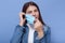 Close up portrai tof attractive female puts on or takes off her mask  over blue background, lady wearing white shirt and