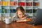 Close-up portrait of adorable cheerful pupil child school girl lying at table with laptop and paper notebook, looking at