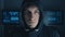 Close up Portrait of Anonymous Hacker programmer in Black Hoody at background of cyber security center filled with