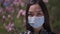 Close-up portrait of Asian young woman in coronavirus face mask opening eyes looking at camera standing in spring park
