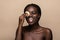 Close up portrait of an attractive african american woman removing makeup with sponge isolated on beige background