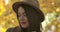 Close-up portrait of attractive European girl in brown hat standing on the background of yellow leaves. Confident