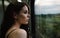 Close-up portrait of an attractive female train passenger standing by the window and looking at the beautiful road scenery. Dreamy