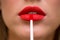 Close up portrait of attractive girl rouging her lips. She is holding red lipstick. Her mouth is gently open. Bright red lip gloss