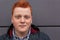 A close-up portrait of attractive redhead freckled boy with round face having stylish haircut wearing trendy clothes posing agains