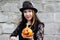 Close-up portrait of attractive woman dressed in Halloween costume against stone wall with Jack-o-lantern.
