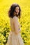 Close up portrait of attractive young woman in canola field. Pretty girl with curly hair posing outdoor on summer day
