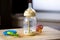 A close up portrait of a baby bottle with a bit of formula still in it standing on a wooden plank. The glass nursing bottle still