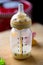 A close up portrait of a baby bottle with a bit of milk still in it standing on a wooden plank. The glass nursing bottle still has