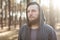 Close up portrait of a bearded hipster tourist in gray hood man in the sunlight woods forest