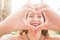 Close up portrait of beautiful.  caucasian young woman doing love hearth sign with hands at the camera - sun bright background and