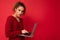 Close-up portrait of beautiful dark blond woman holding laptop computer looking at camera typing on keyboard wearing red