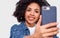 Close up portrait of beautiful dark skinned young woman in white t-shirt and blue shirt, taking selfie over white studio wall