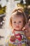 Close up portrait of beautiful small baby, blond little girl in colourful pullover in mothers hands in park outdoors