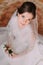 Close-up portrait of beautiful smiling bride in wedding dress sitting on carpet and holding cute floral boutonniere
