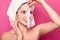 Close up portrait of beautiful young girl with naked shoulders poses at pink background, removes facial mask, skin care concept,