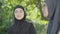 Close-up portrait of beautiful young Muslim woman in black hijab talking with blurred friend and smiling. Charming