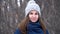 Close-up portrait of beautiful young smiling caucasian woman in winter jacket, hat and scarf. Brunette girl snowy wood