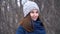 Close-up portrait of beautiful young smiling caucasian woman in winter jacket, hat and scarf. Brunette girl snowy wood