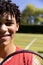 Close-up portrait of biracial young man with tennis racket smiling in tennis court on sunny day