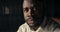 Close-up portrait of a Black-skinned man in a white shirt who looks at the camera and does not smile