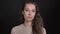 Close-up portrait of brunette long-haired caucasian girl approvingly nodding into camera on black background.