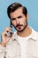 Close-up portrait of a brunette man talking on the phone, disgruntled and angry, on a blue background in a white T-shirt