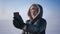 Close-up portrait of businessman in warm coat and hood having a videocall on smartphone in snow desert.