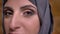 Close-up portrait of calm middle-aged muslim woman in hijab with bright make-up watching into camera on bricken wall