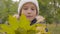 Close-up portrait of a Caucasian girl in white hat holding a bunch of yellow leaves and smiling. Pretty young lady