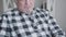 Close-up portrait of Caucasian grey-haired sad man sitting indoors and thinking. Camera moving up from hands holding