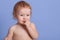 Close up portrait of charming little boy biting his fingers, looking at camera, posing isolated over blue studio background. Naked