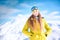 Close up portrait of cheerful girl snowboarder in yellow jacket in front of snowy mountains