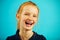 Close-up portrait of cheerful laughing girl with red hair and freckles on blue isolated background. Happy child