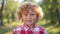 Close-up portrait of cheerful redhead little boy with curly hair looking at camera smiling standing in sunshine outdoors